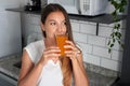 Girl drinking tangerine juice in kitchen. Young woman drinking orange or carrot fresh vitamin juice in the morning at home Royalty Free Stock Photo