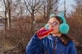 Girl drinks from a bottle in the street. A teenage girl in headphones and glasses