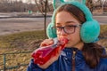 Girl drinks from a bottle in the street. A teenage girl in headphones and glasses