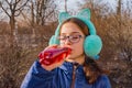 Girl drinks from a bottle in the street. A teenage in headphones and glasses drinks a fruit drink