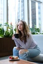 a girl drinks coffee with pleasure from a black cup sits near the window in the hall plants in the background Royalty Free Stock Photo
