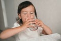 The girl drinks water from a glass glass. A little girl quenches her thirst. Proper nutrition for children. Snack for an