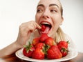 Girl eagerly eating strawberries on white background