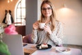 Girl eating cake in a cafe. Blonde in polka-dot shirt with laptop Royalty Free Stock Photo