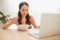 Girl eating instant noodle in hurry time while running her business at home on notebook computer Royalty Free Stock Photo