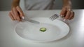 Girl eating one small piece of cucumber, harming health, fear of overweight