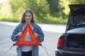 A girl with an emergency sign stands near a car that was involved in an accident
