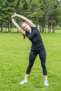 The girl is engaged in fitness in the park. Tilts with arms raised