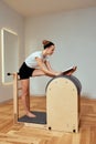 A girl is engaged in Pilates on the reformer reading a book, Pilates classes on the reformer, strengthening the Royalty Free Stock Photo