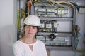 A girl in an engineering helmet is on the background of a fuse box.Portrait of an electrician in a white helmet next to high-