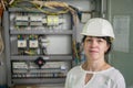 A girl in an engineering helmet is on the background of a fuse box.Portrait of an electrician in a white helmet next to high-