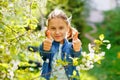 The girl is enjoying the apple blossom. A little school-age girl in a garden with tree flowers. Shows two thumbs up Royalty Free Stock Photo