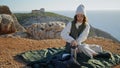 Girl enjoying cliff picnic alone. Curly tourist admiring ocean landscape resting