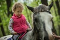 Girl enjoying horseback riding in the woods, young pretty girl with blond curly hair on a horse with backlit leaves Royalty Free Stock Photo