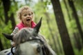 Girl enjoying horseback riding in the woods, young pretty girl with blond curly hair on a horse with backlit leaves Royalty Free Stock Photo