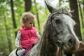 Girl enjoying horseback riding in the woods, young pretty girl with blond curly hair on a horse with backlit leaves Royalty Free Stock Photo