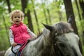 Girl enjoying horseback riding in the woods, young pretty girl with blond curly hair on a horse with backlit leaves Royalty Free Stock Photo