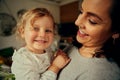 Small preschool cute girl smiling looking at camera on mother hands at home