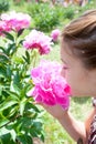 Girl enjoying of pink Minuet peony smell in formal garden