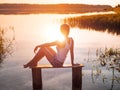 The girl enjoys a beautiful sunset sitting on a bench by the river. Girl sitting near water outdoors. Golden sunset lake Royalty Free Stock Photo