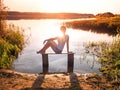 The girl enjoys a beautiful sunset sitting on a bench by the river. Girl sitting near water outdoors. Golden sunset lake Royalty Free Stock Photo