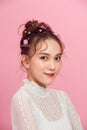 The girl with everyday makeup and hair in wedding bun with flowers on pink background