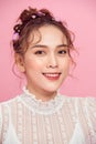 The girl with everyday makeup and hair in wedding bun with flowers on pink background