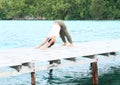 Girl exercising yoga pose downward-facing dog on jetty by sea