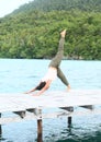 Girl exercising yoga pose three-legged downward dog on jetty by sea