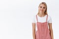 Girl facing bummer, lose competition and sighing. Attractive blond woman in pink overalls, t-shirt, smirk and tilt head Royalty Free Stock Photo