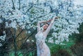 A girl with fair hair, in a transparent dressing-gown posing against a background of blooming, white magnolia. Spring, gentle port