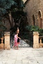 The girl in the fairy-tale crown steps towards the garden behind the forged ancient fence Royalty Free Stock Photo