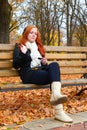 Girl in fall season listen music on audio player with headphones, sit on bench in city park, yellow trees and fallen leaves Royalty Free Stock Photo