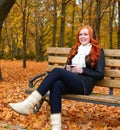 Girl in fall season listen music on audio player with headphones, sit on bench in city park, yellow trees and fallen leaves Royalty Free Stock Photo