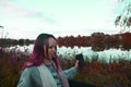 A girl in the fall sits by the lake on a blanket, with a cup of coffee. Autumn girl watching nature. Autumn forest