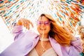 A girl at the festival looks at the camera and smiles against the background of a colorful background, dancing in purple glasses Royalty Free Stock Photo