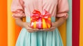 A girl in a festive bright dress holds a gift box in her hands, wrapping paper and ribbons shimmer with candy shades