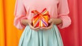 A girl in a festive bright dress holds a gift box in her hands, wrapping paper and ribbons shimmer with candy shades