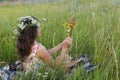 Girl in the field. Side view of a sitting girl with long hair in a wreath of wildflowers.