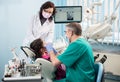 Girl with on the first dental visit. Senior pediatric dentist with nurse treating patient teeth at the dental office