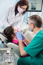 Girl with on the first dental visit. Senior pediatric dentist with nurse treating patient teeth at the dental office