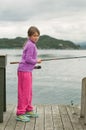 A girl with a fishing rod standing on the wooden deck near water Royalty Free Stock Photo