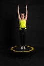 Girl on a fitness trampoline on a black background in a yellow t-shirt black energy woman, fun exercise caucasian health Royalty Free Stock Photo