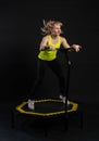 Girl on a fitness trampoline on a black background in a yellow t-shirt trampoline fit woman, active activity female girl Royalty Free Stock Photo