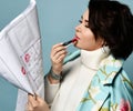 Girl in floral print coat. She puts red lipstick on her lips and kissing blueprint of house, posing sideways on blue background Royalty Free Stock Photo