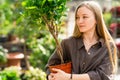 Girl florist with a plant in a pot in her hand looks to the side.