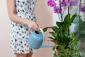 The girl florist watered the house plants from the watering can. On the window-sill is a pot of orchid, zamioculcas and dieffenbac