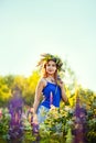 A girl with a flower wreath on her head sits at sunset in a field with purple lupin flowers. Image with selective focus  toning Royalty Free Stock Photo