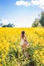 girl with flowers and a hat in her hand runs into a field of rapeseed. Yellow flower field. View from the back Royalty Free Stock Photo