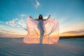 A girl in a fly white dress dances and poses in the sand desert at sunset Royalty Free Stock Photo